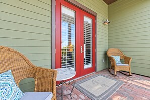 A covered porch with two wicker chairs, a small table, and a red door with glass panels.