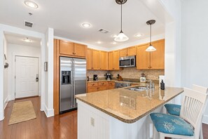 A modern kitchen with wooden cabinets, stainless steel appliances, granite countertops, and pendant lighting.