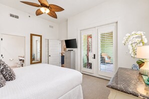 Une chambre à coucher comprenant un lit, un ventilateur de plafond, un téléviseur et une porte coulissante donnant sur un balcon.