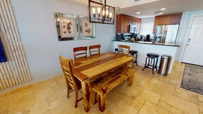 Een eetruimte met een houten tafel en stoelen, een bank, een keuken met moderne apparatuur en kunstwerken in lijsten aan de muur.