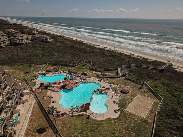 Luchtbeeld van een resort met meerdere zwembaden, een strand en een boardwalk.