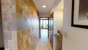 Un couloir avec un mur recouvert de carreaux, une porte donnant sur un balcon et un tableau encadré accroché au mur.