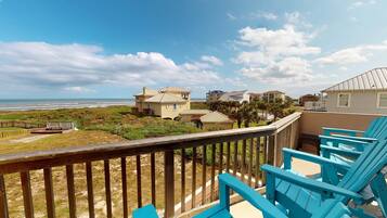 A beachfront property with a wooden deck and blue chairs, overlooking the ocean and neighboring houses.
