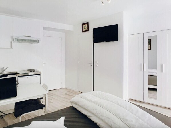 A bedroom with a bed, a desk with a computer, a TV, and a wardrobe.