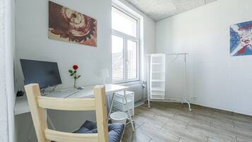 Ein Zimmer mit Schreibtisch, Computer, Stuhl, Heizkörper und Bildern an den Wänden.