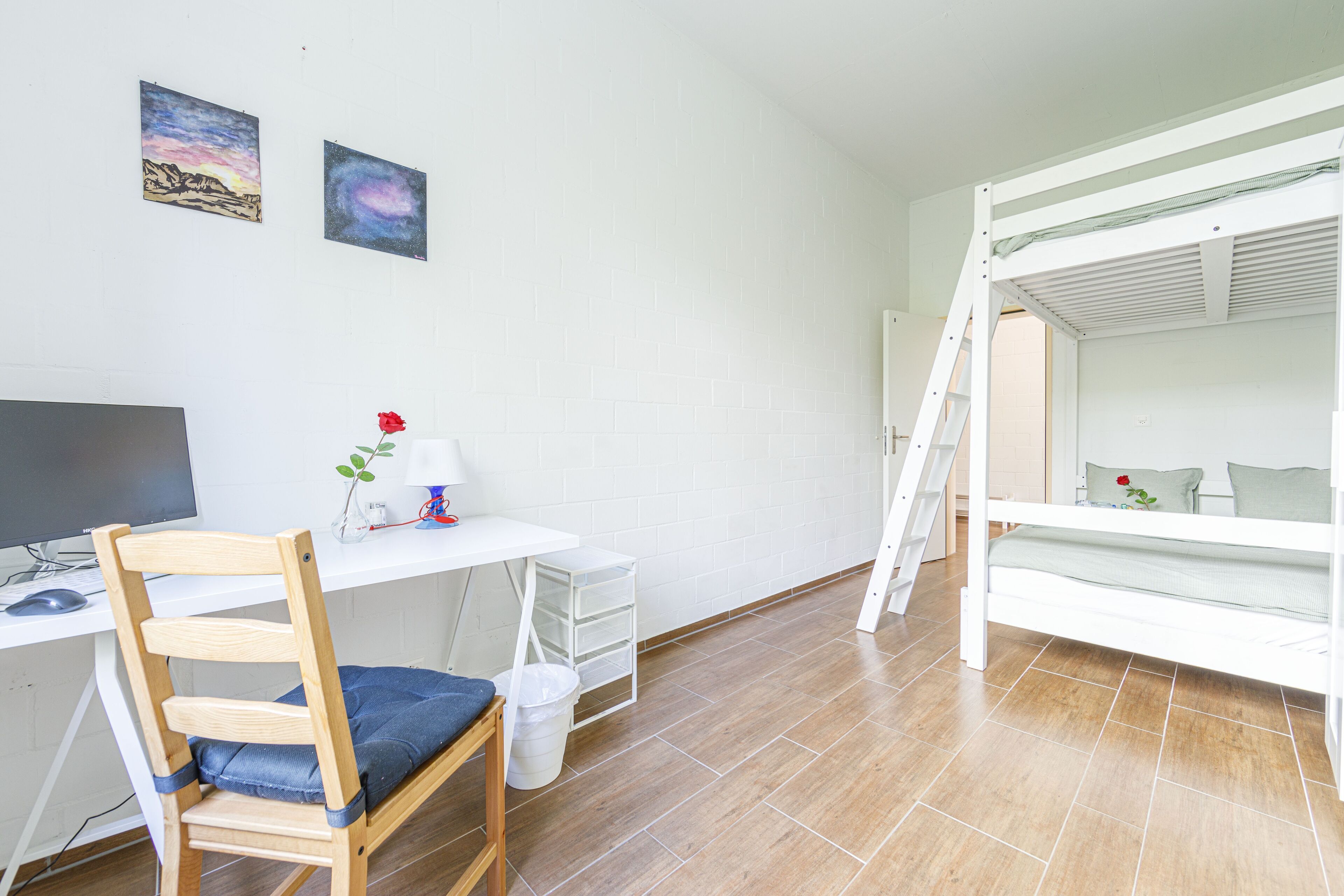 Een kamer met een stapelbed, een bureau met een computer, een stoel en twee decoratieve wandobjecten.