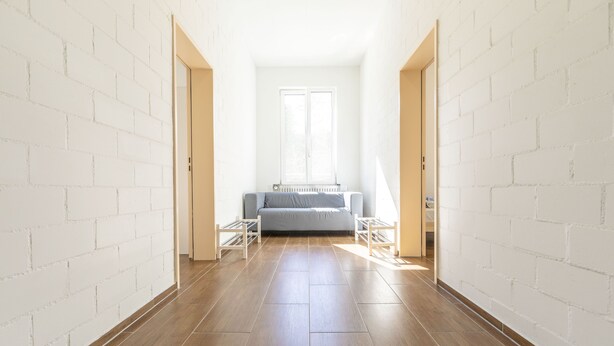 A hallway with a wooden floor, white brick walls, and a grey sofa in the background. - Yellow Inn (St. Gallen)
