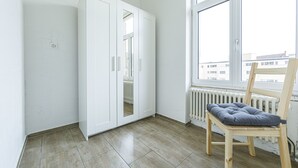 A room with a white wardrobe, a radiator, a window, and a wooden chair with a cushion. - Yellow Inn (St. Gallen)