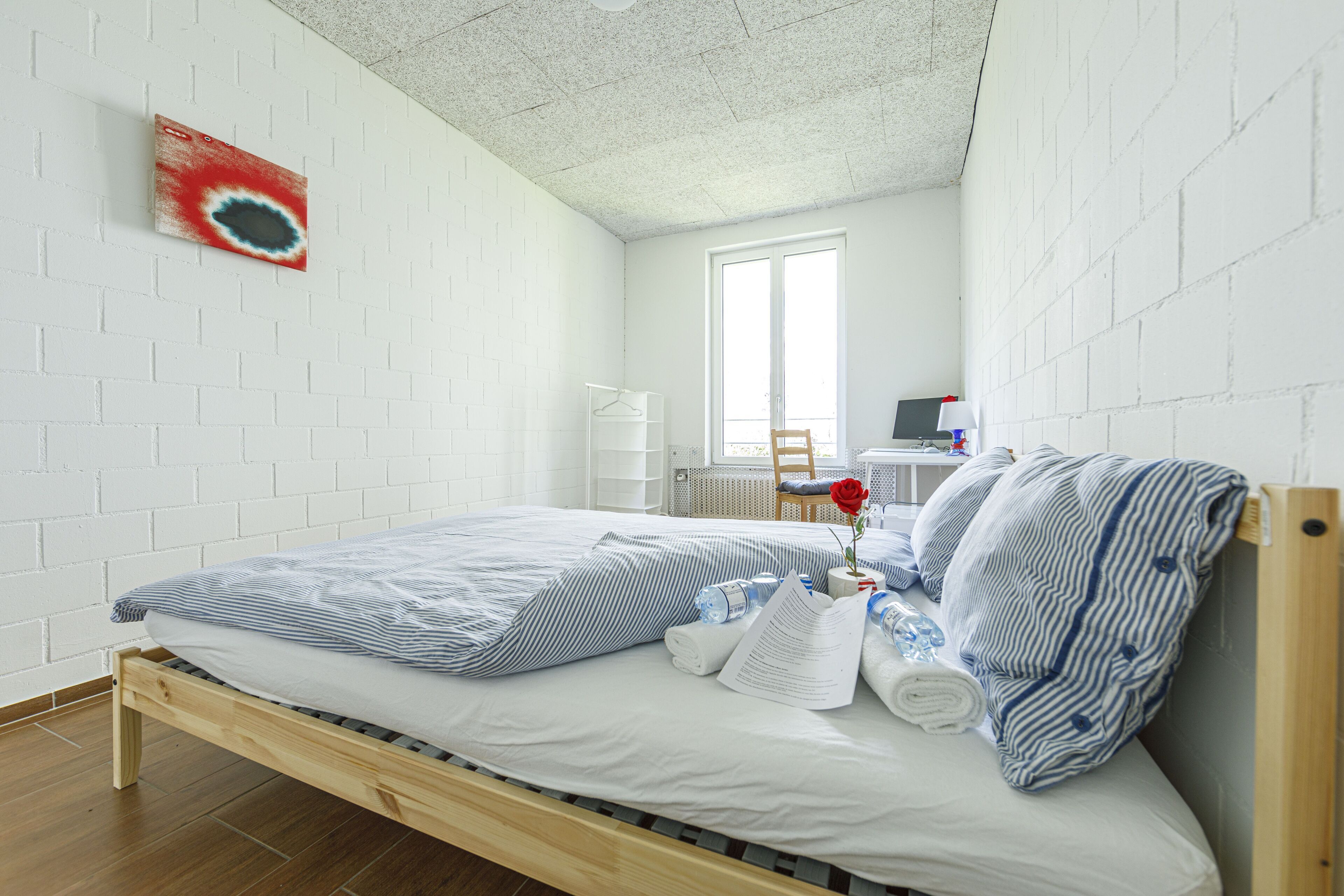 A neatly made bed with striped bedding, a wooden headboard, and a small bedside table with a lamp and a book.