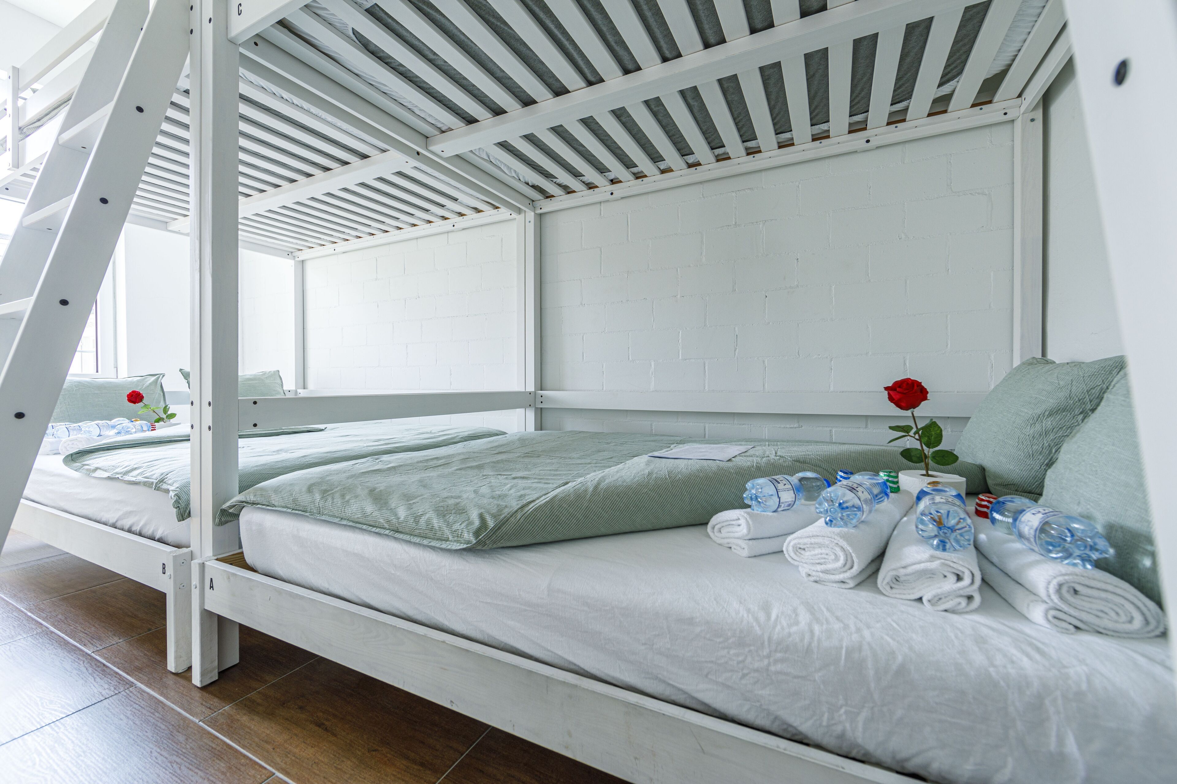 A bunk bed with white bedding, a rose on the bed, and rolled towels on the side.