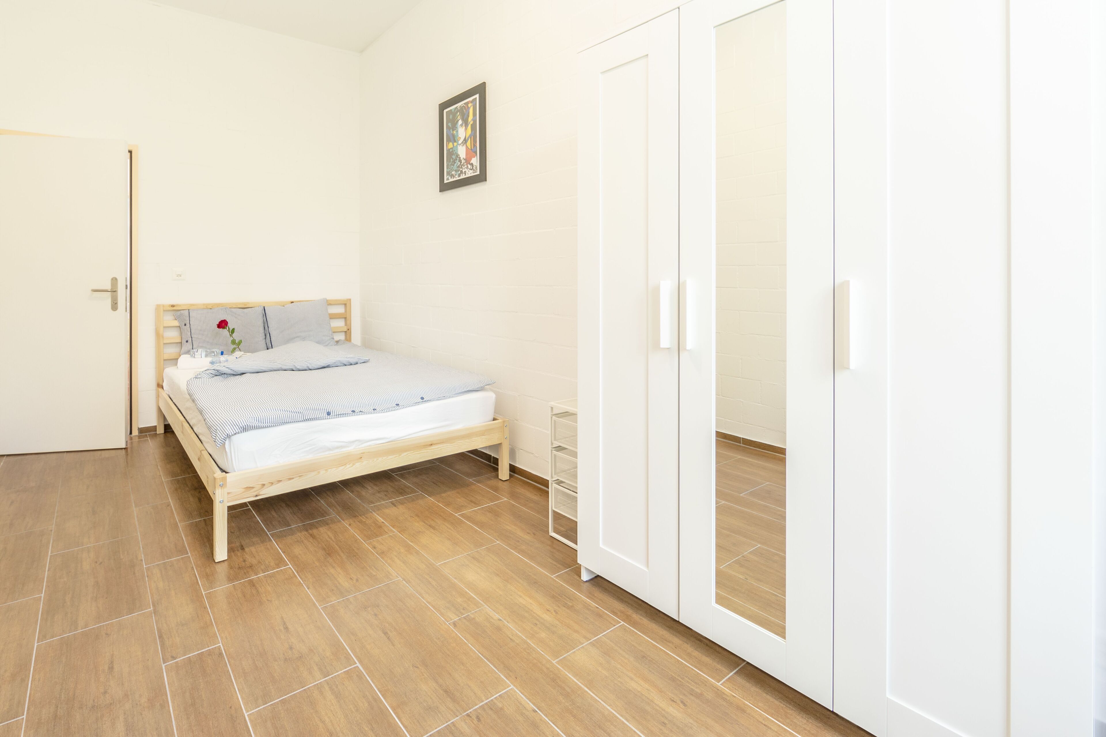 Een slaapkamer met een houten bed, een witte kledingkast en een klein nachtkastje.