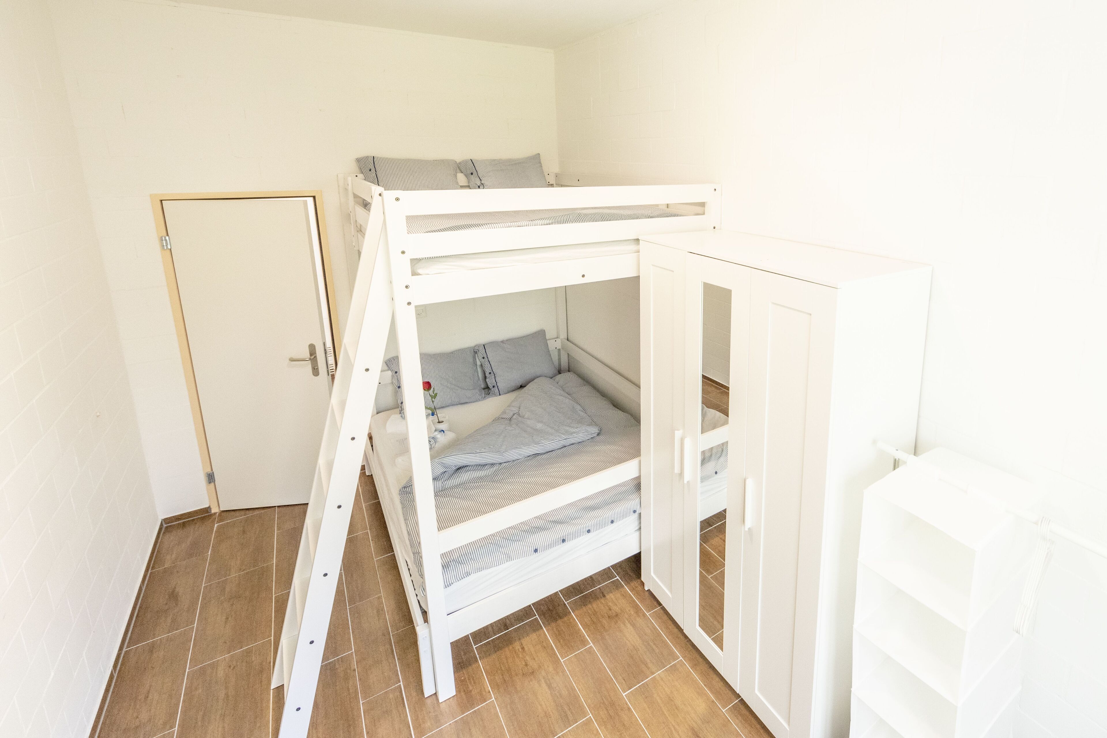 A bunk bed with a wardrobe, a door, and a tiled floor.