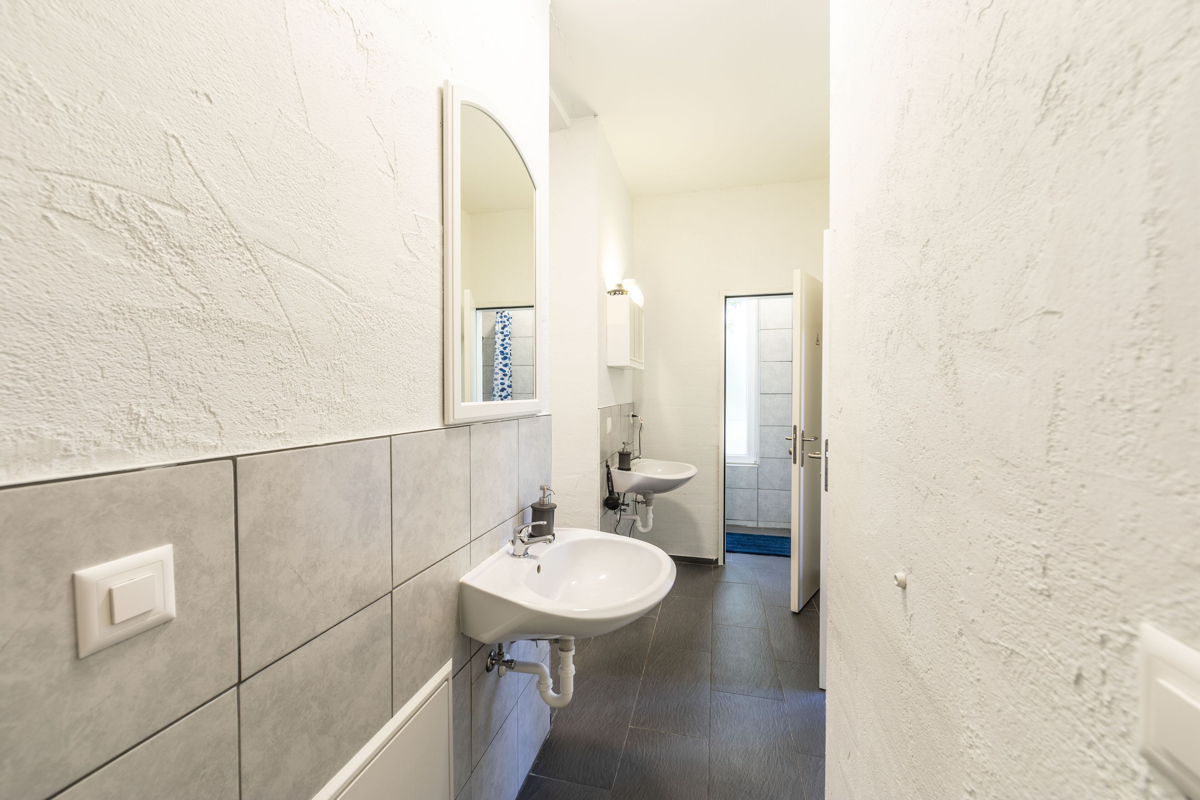 Un baño estrecho con dos lavamanos, un espejo y una puerta que da a otra habitación.