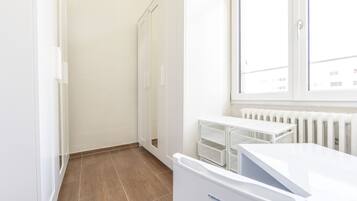 Ein sauberer, weiß gestrichener Raum mit Heizkörper, Fenster und weißem Schrank.