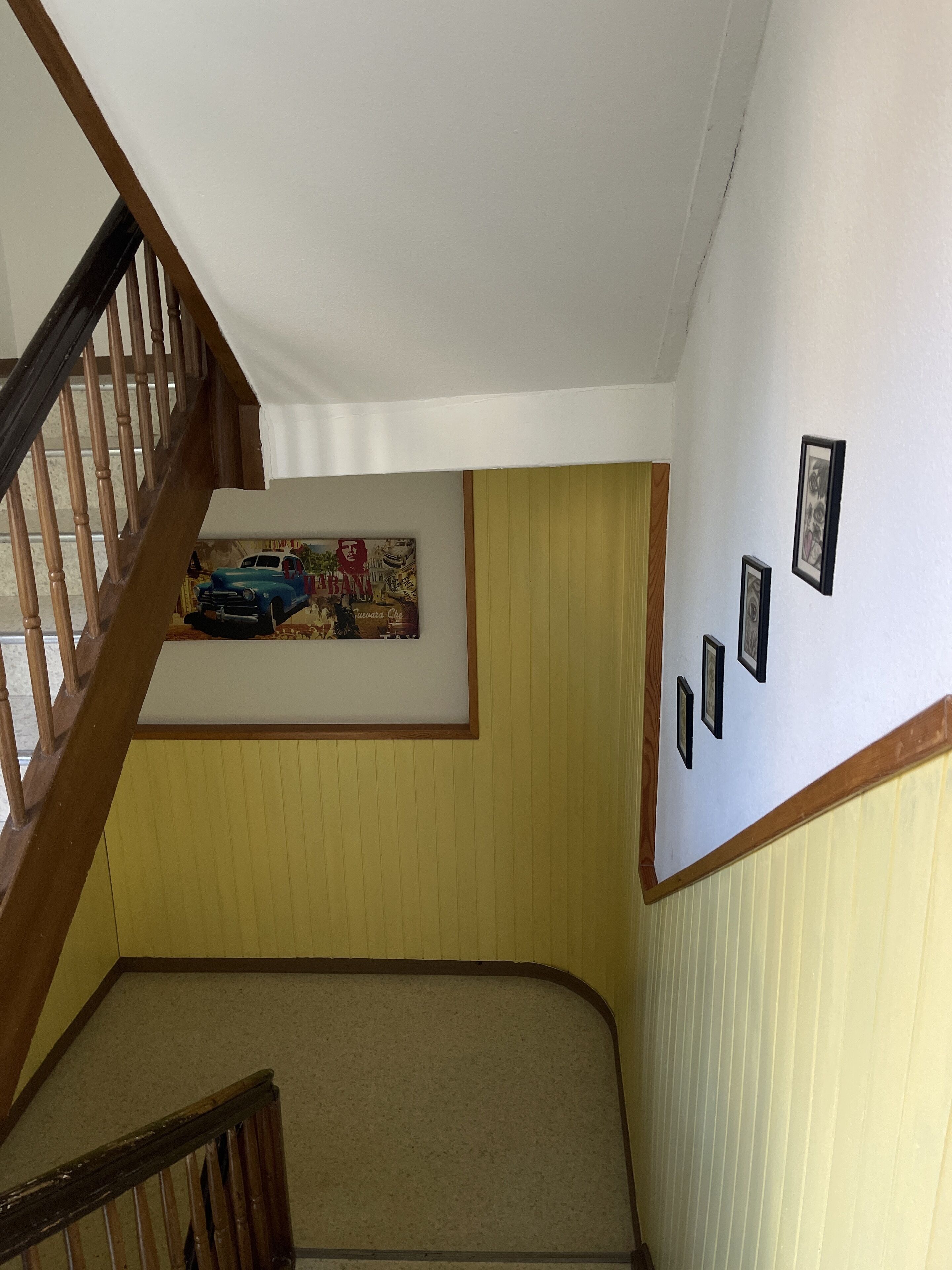 A staircase with wooden railings leading to a landing with a beige carpet. A wall-mounted picture frame with a vintage car illustration is visible.
