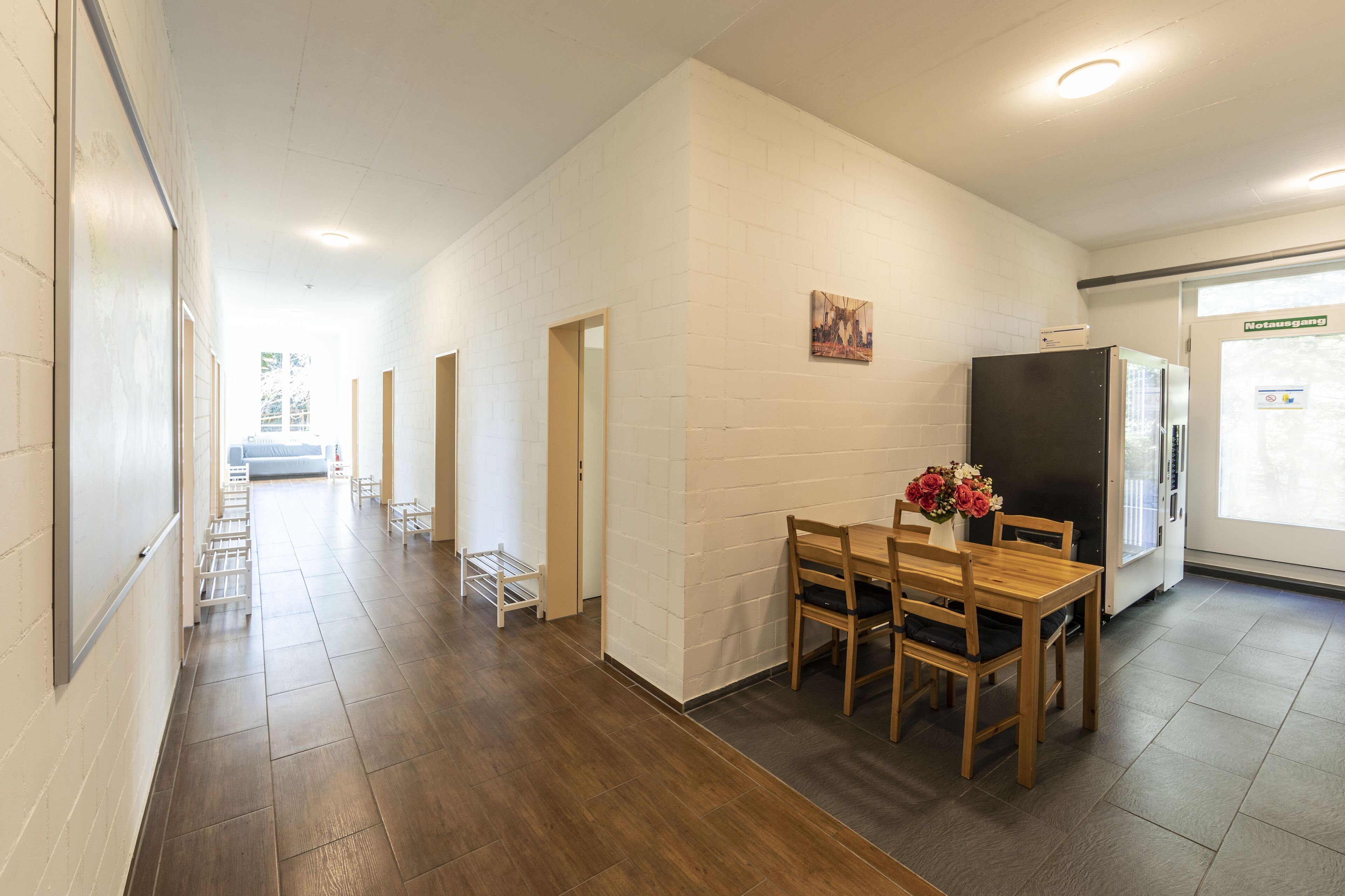 A hallway with a wooden floor, white brick walls, and a dining area with a table and chairs.