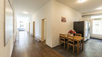 A hallway with a wooden floor, white brick walls, and a dining area with a table and chairs.
