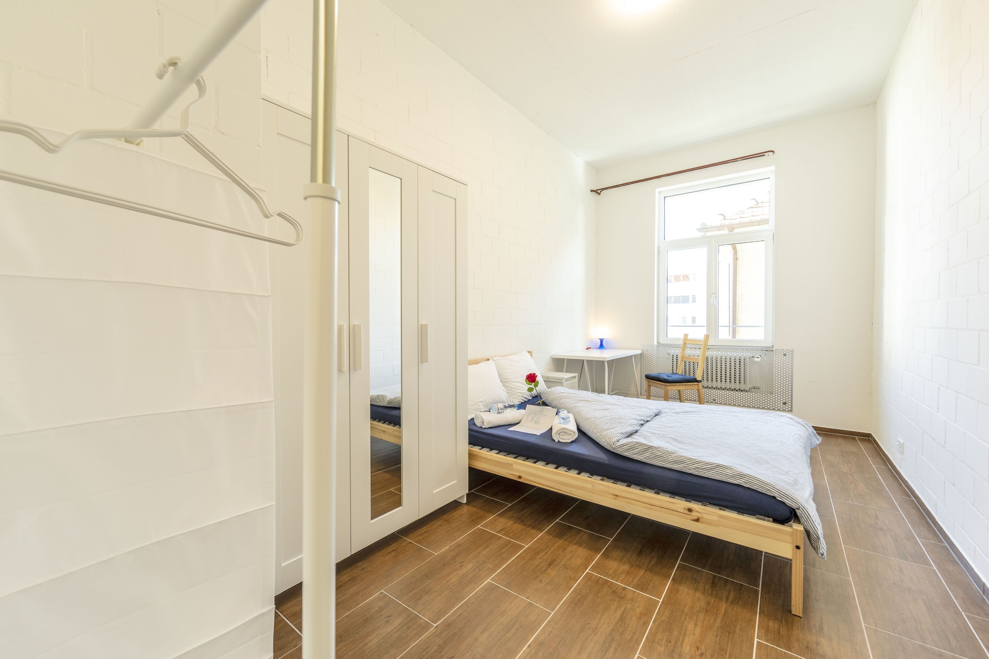 A bedroom with a bed, a desk, a chair, and a radiator.