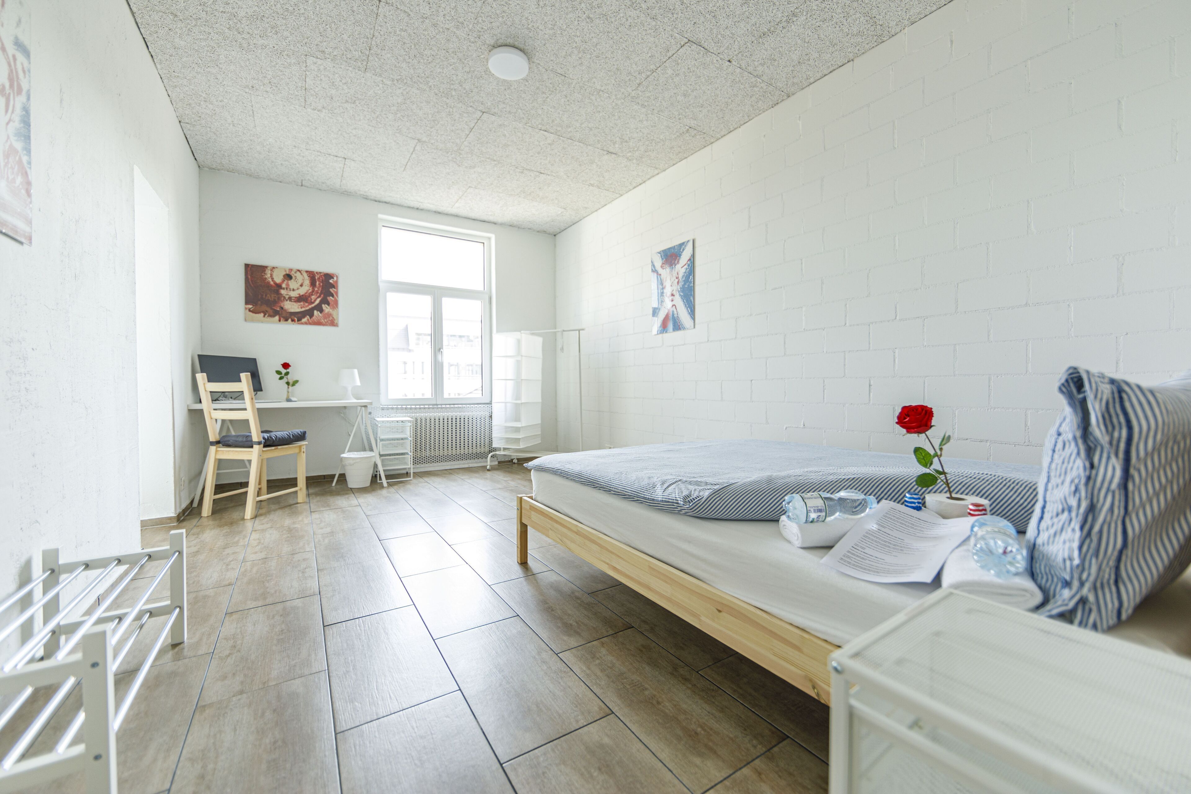 Ein schlicht eingerichteter Raum mit Bett, Schreibtisch und Stuhl. Ein Fenster sorgt für natürliches Licht, und an der Wand ist eine Heizung erkennbar.