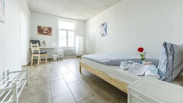 Ein schlicht eingerichteter Raum mit Bett, Schreibtisch und Stuhl. Ein Fenster sorgt für natürliches Licht, und an der Wand ist eine Heizung erkennbar.