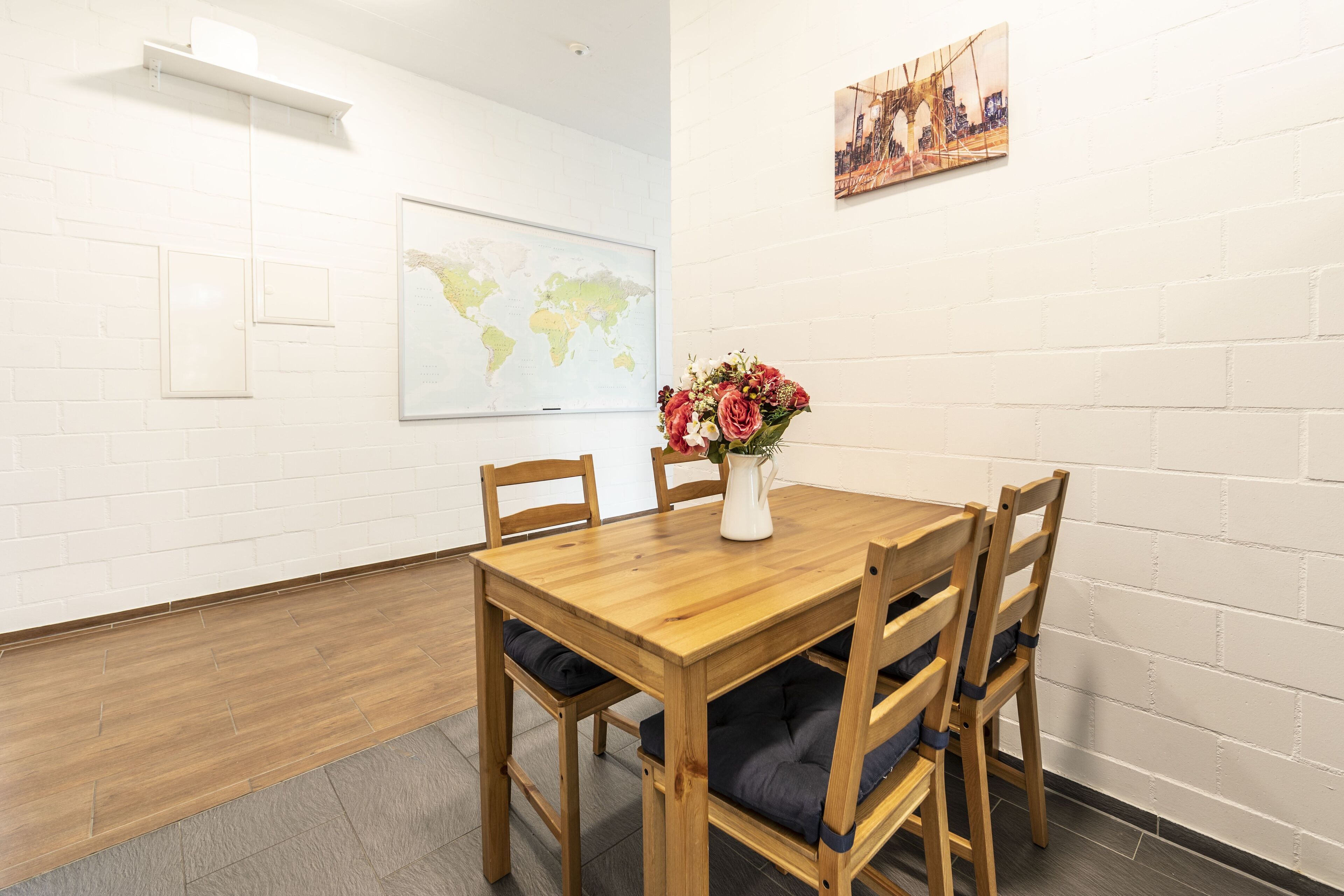 Une table à manger en bois, avec quatre chaises, un vase rempli de fleurs et une carte du monde accrochée au mur.