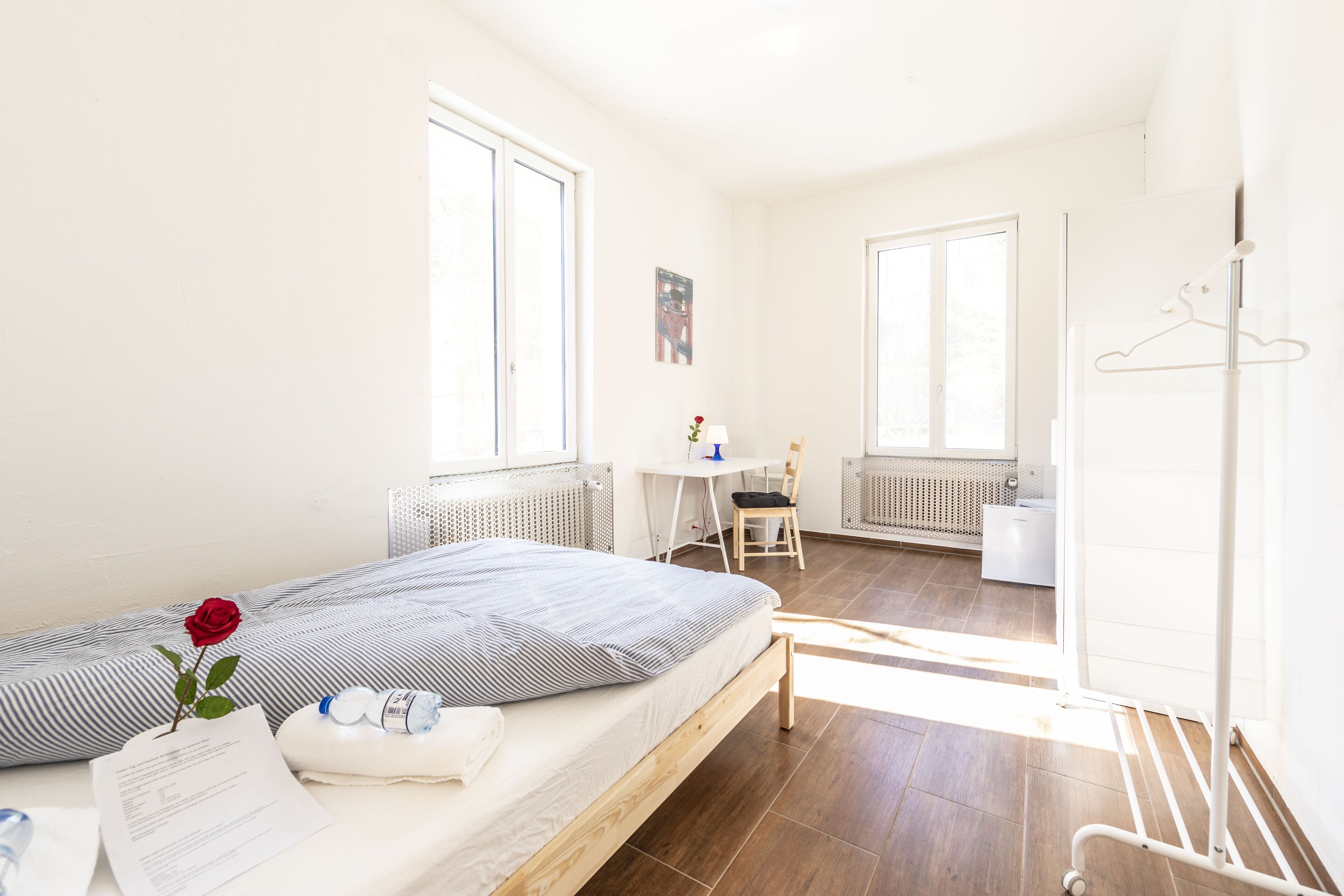 A bedroom with a bed, a desk, a chair, a radiator, and a window.