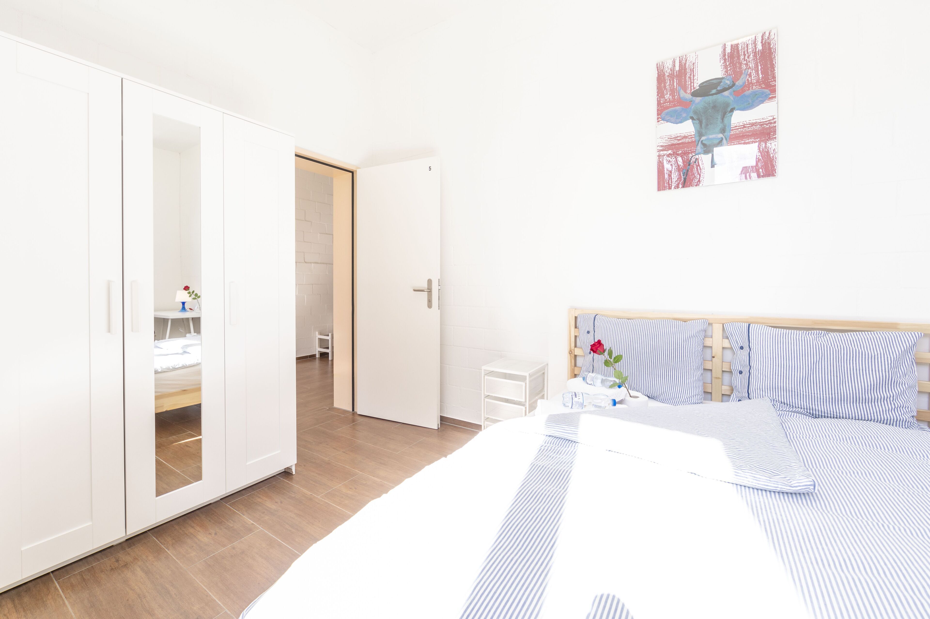 Ein Schlafzimmer mit einem Bett, einem Kleiderschrank, einem Nachttisch und einem Bild an der Wand.