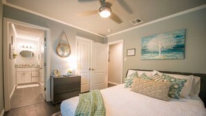 Un dormitorio con cama, cómoda, espejo, ventilador de techo y un cuadro en la pared.