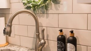 Una cocina con un lavamanos de acero inoxidable, un grifo plateado y dos botellas de jabón en la encimera.