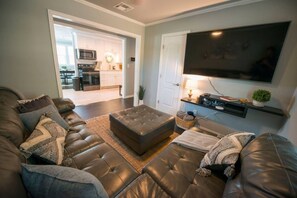 Ein Wohnzimmer mit Ledersofa, Flachbildfernseher und einer Küche im Hintergrund.