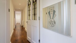 A hallway with a wooden floor, a white door with stained glass, and a wall-mounted sign that reads "THE FLEA PIT".