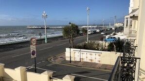 A coastal street with a speed limit sign, a pay and display zone, and a view of the sea and a pier in the background.