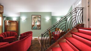 A staircase with red carpet and metal railings, a dining area with a table and chairs, and a painting on the wall.