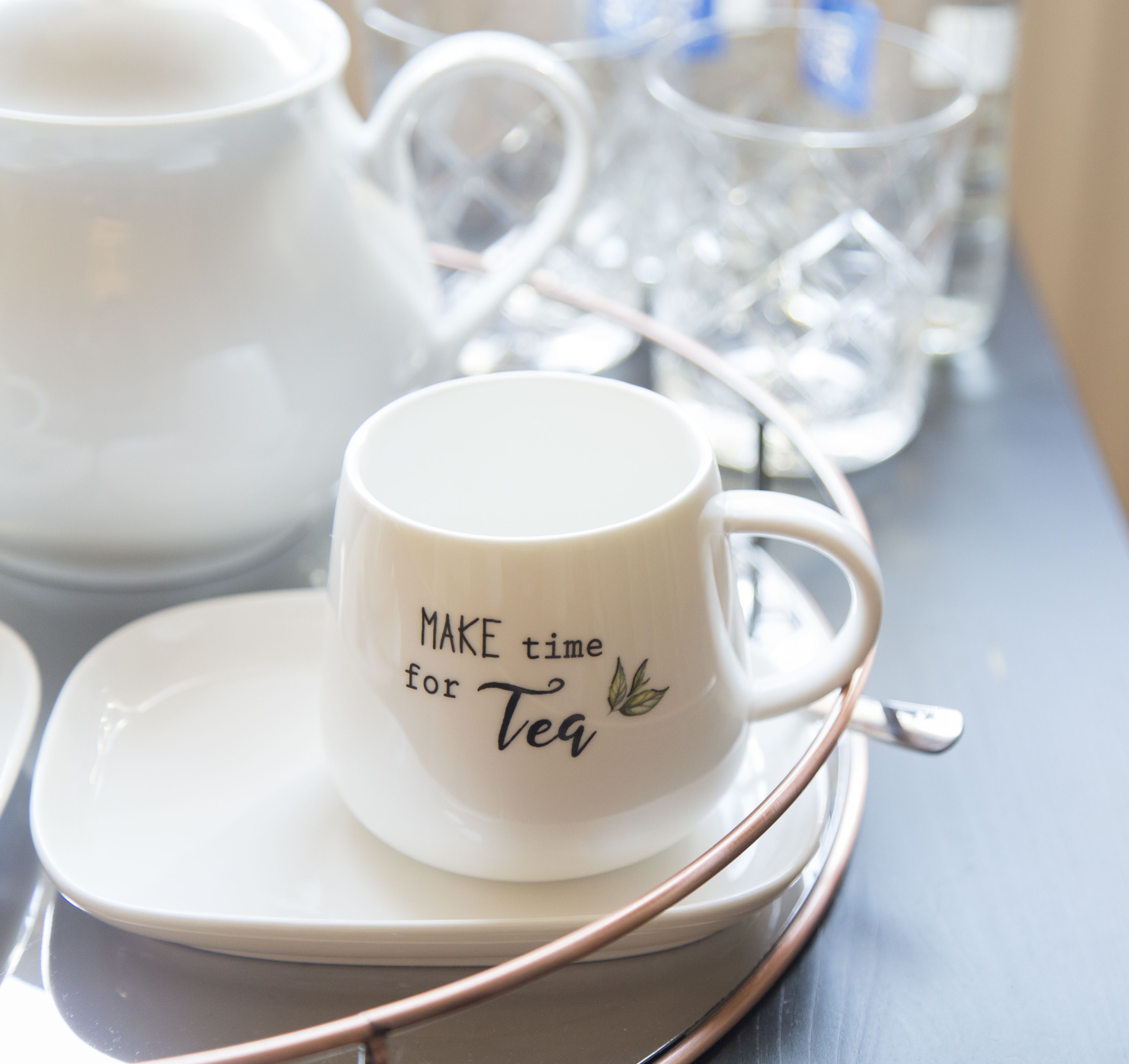 Una taza blanca con su platillo y una bandeja para té con tetera y vasos.