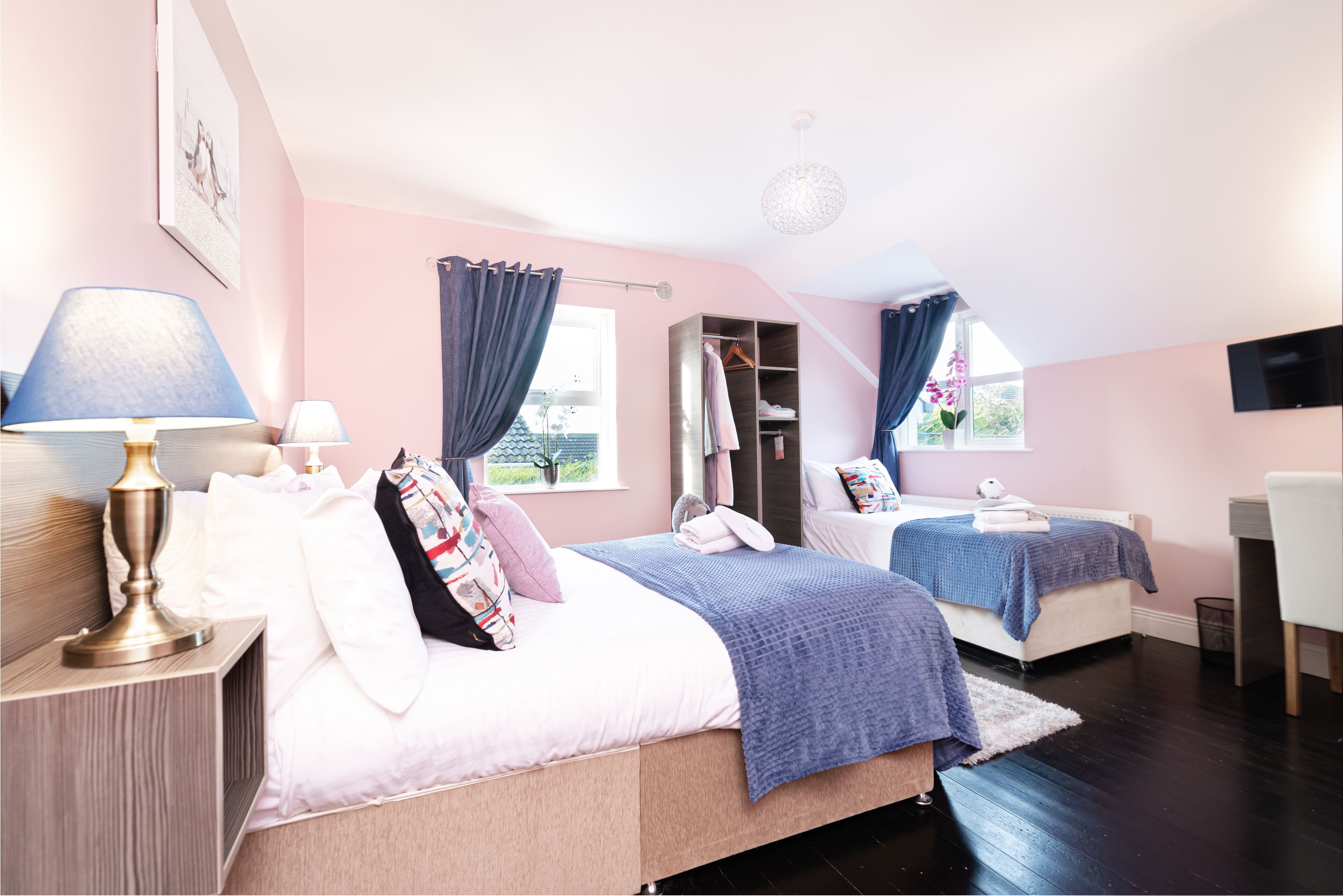 A bedroom with two beds, a wardrobe, a desk, and a TV.
