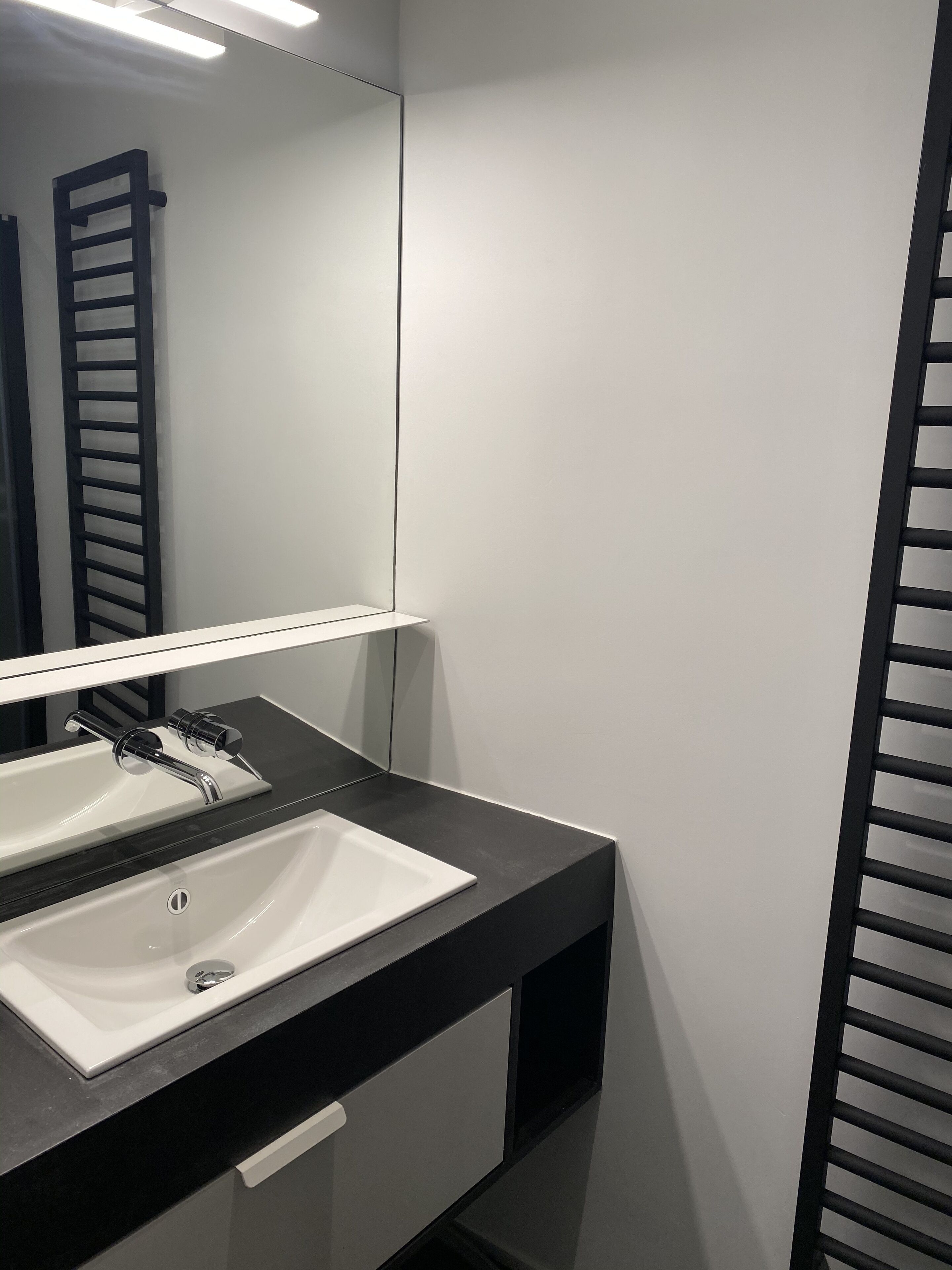 Un baño moderno con un lavamanos blanco, encimera negra y un espejo encima.