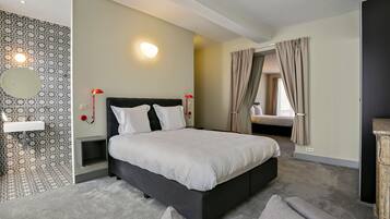 Una habitación de hotel moderna con una cama grande, una mesita de noche, un espejo y un baño con pared decorada.