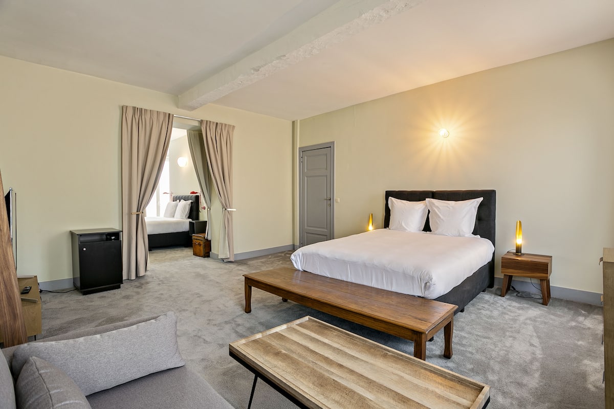 Una habitación de hotel con una cama grande, un banco de madera, un sofá, un escritorio y una mesita.