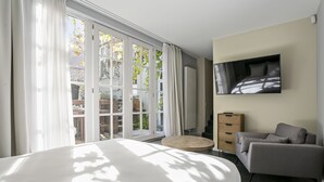 A bedroom with a large bed, a TV mounted on the wall, a grey sofa, and a wooden cabinet. - Fishmarket B&B (Brussels)
