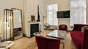 A modern living room with a fireplace, red furniture, a glass coffee table, and a large mirror. - Fishmarket B&B (Brussels)