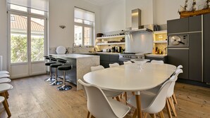 A modern kitchen with a large island, white dining table, and bar stools. - Fishmarket B&B (Brussels)