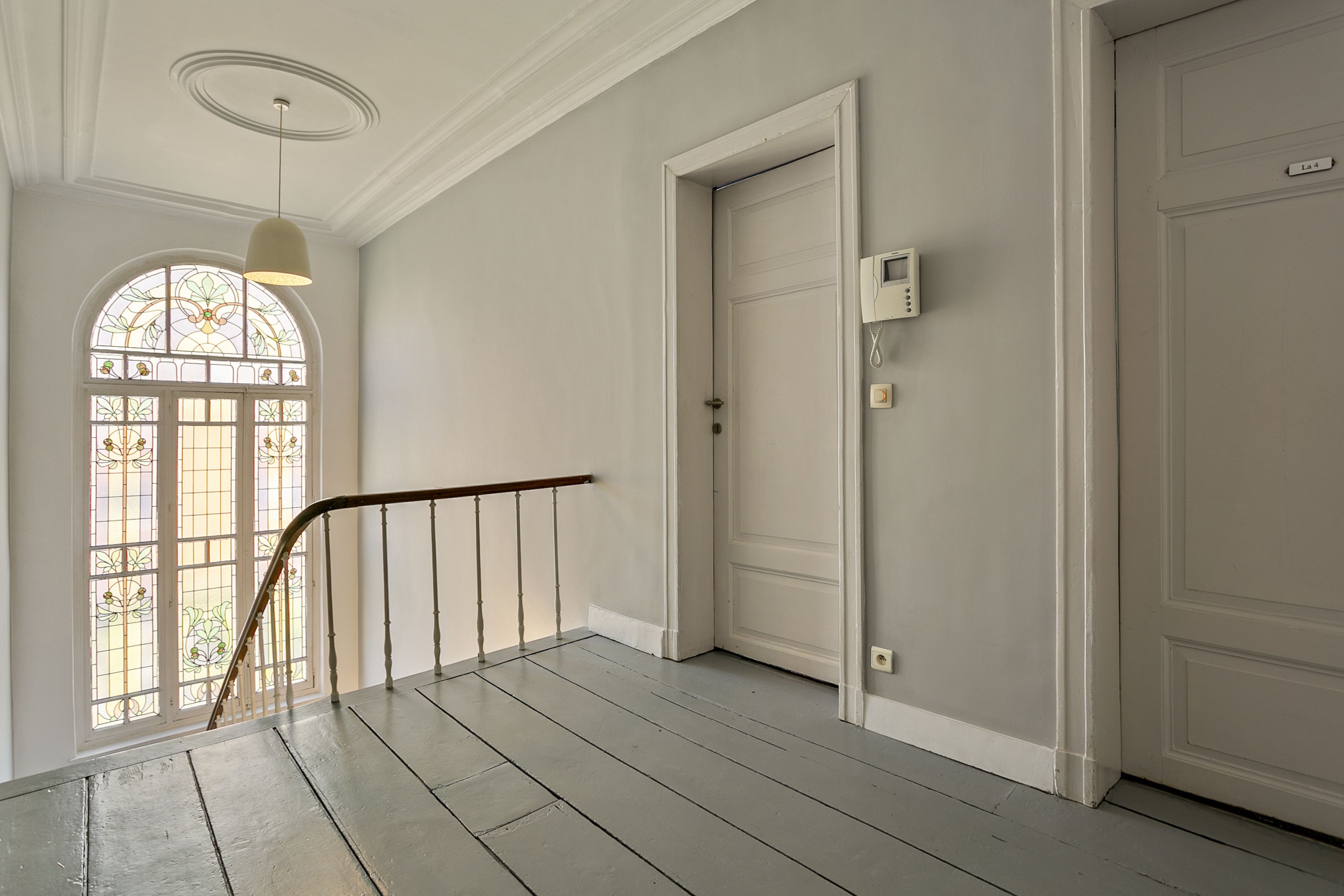 A hallway with a wooden staircase, a white door with a security panel, and a stained glass window.