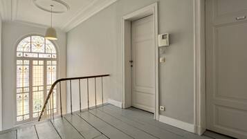 A hallway with a wooden staircase, a white door with a security panel, and a stained glass window.