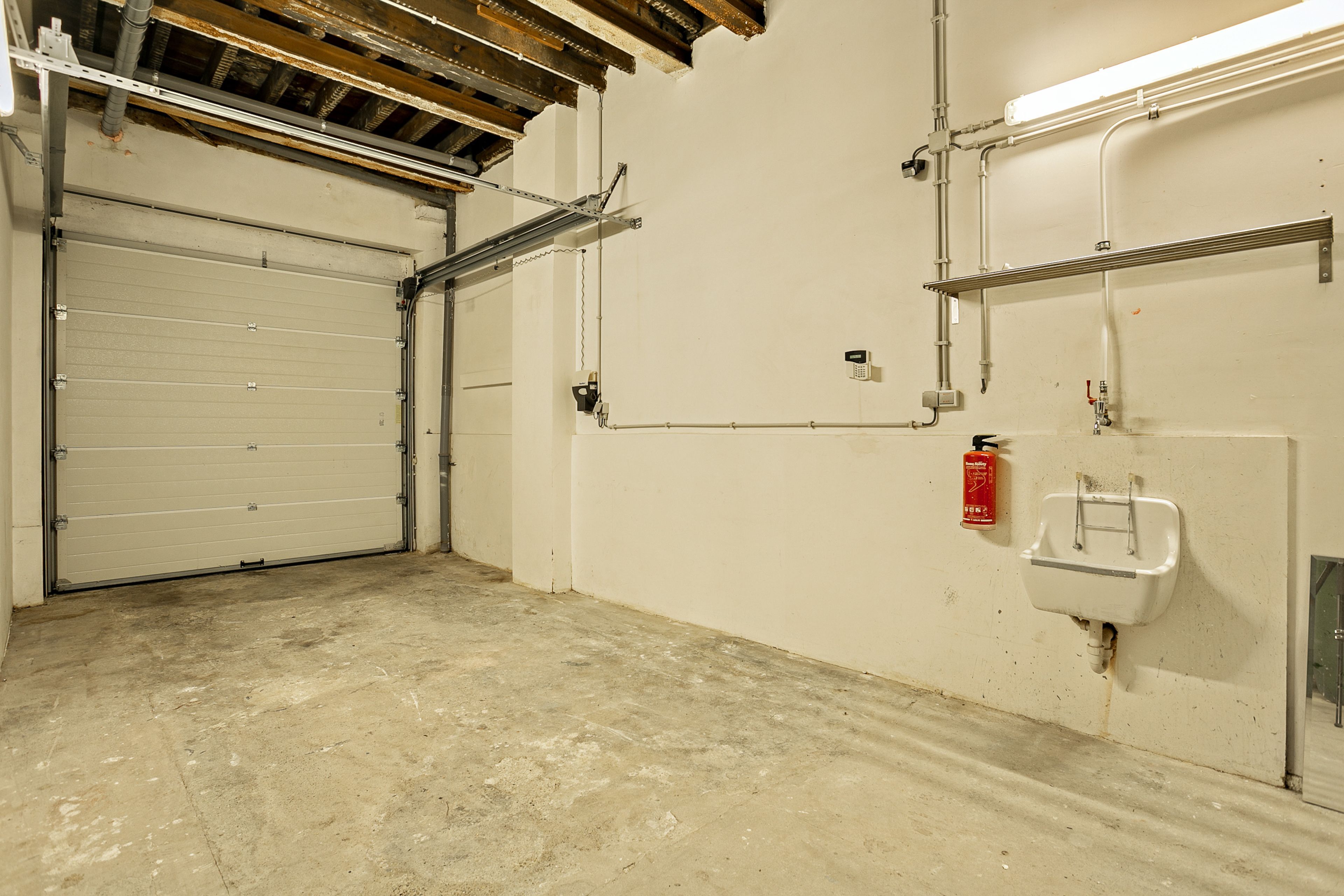 A clean, empty garage with a closed garage door, a fire extinguisher, and a wall-mounted sink.