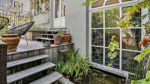A wooden deck with steps leading to a window overlooking a garden. - Fishmarket B&B (Brussels)