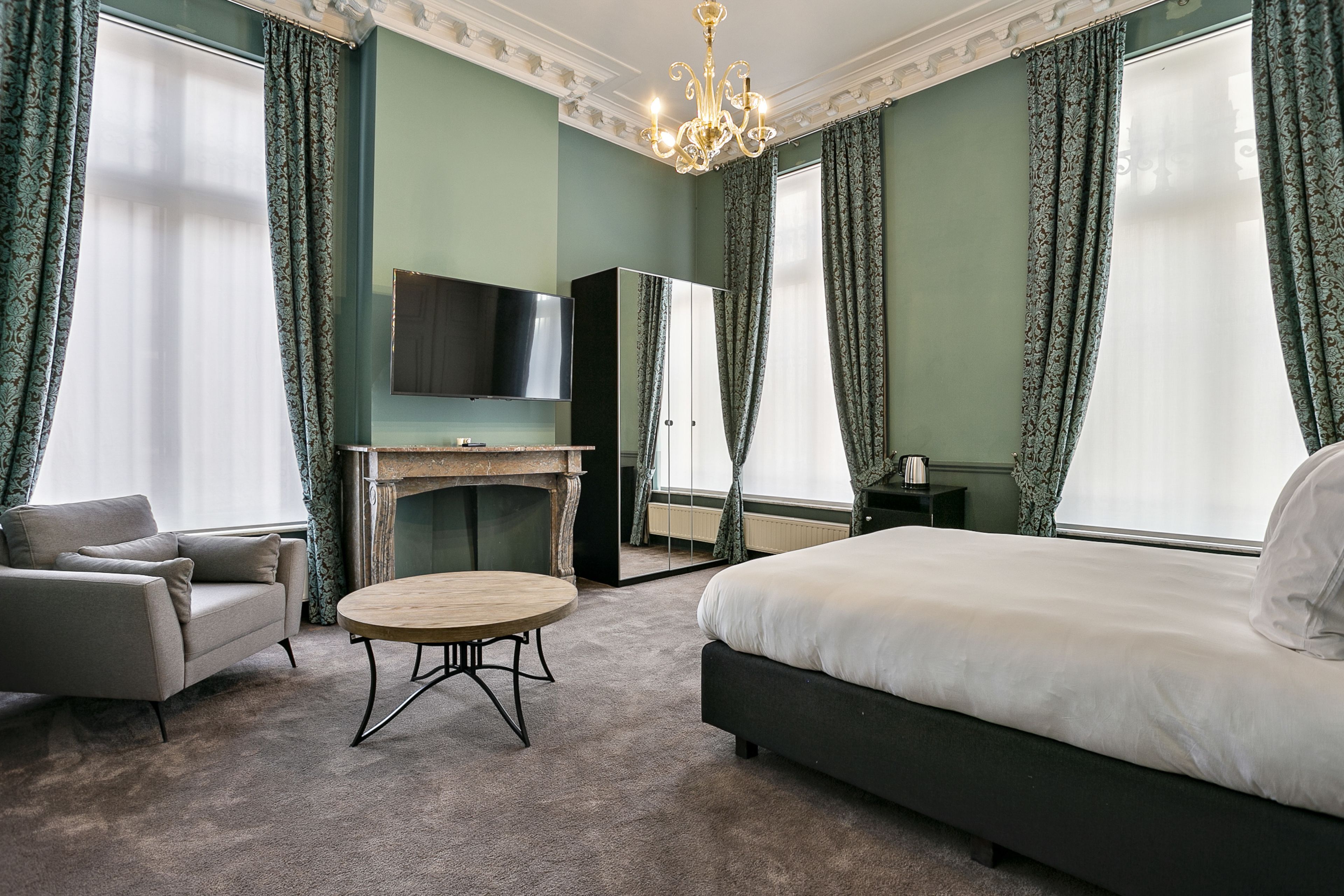 A bedroom with a bed, a sofa, a round table, a TV, and a fireplace.