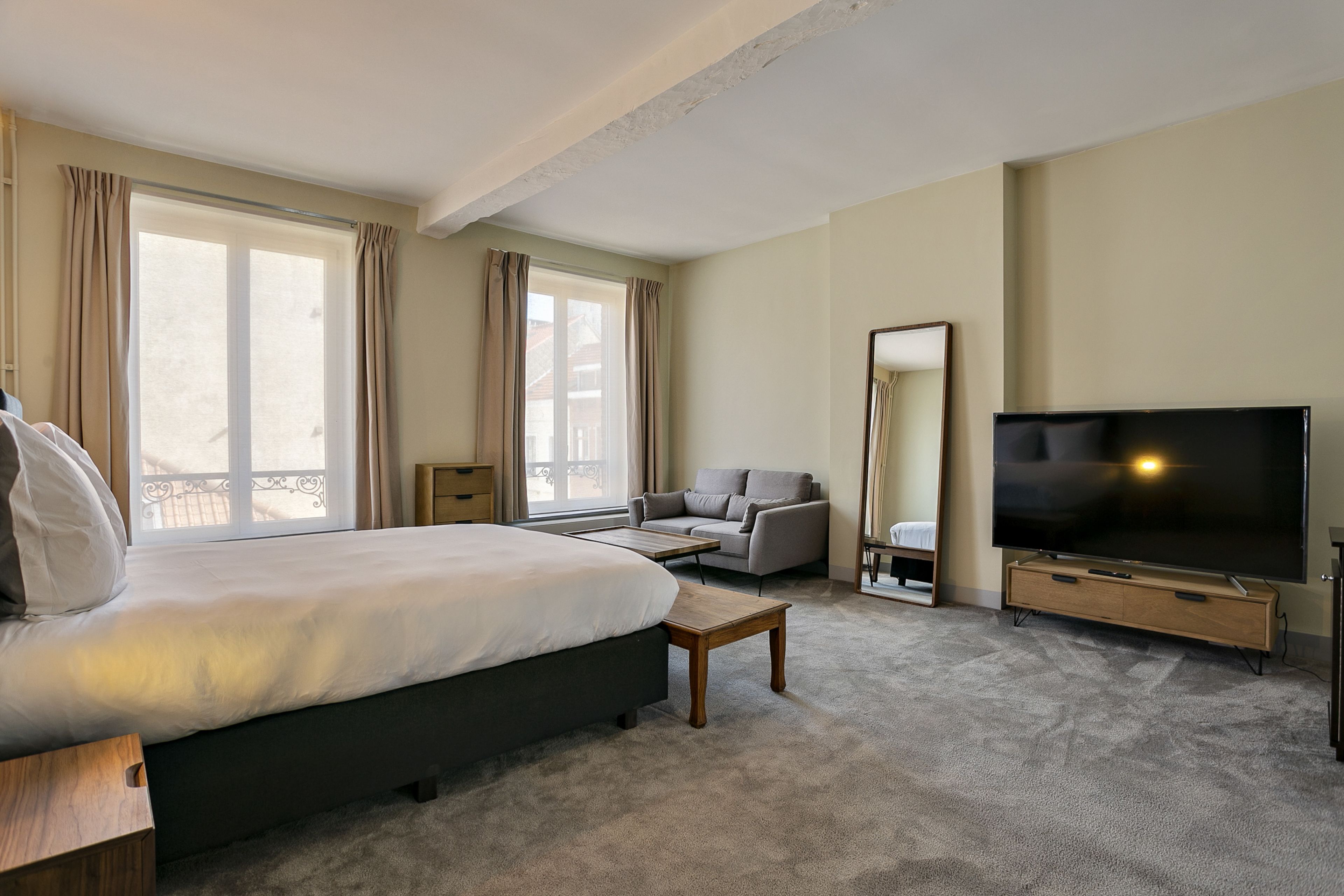 Una habitación de hotel con una cama grande, un sofá, un televisor y una ventana con cortinas.