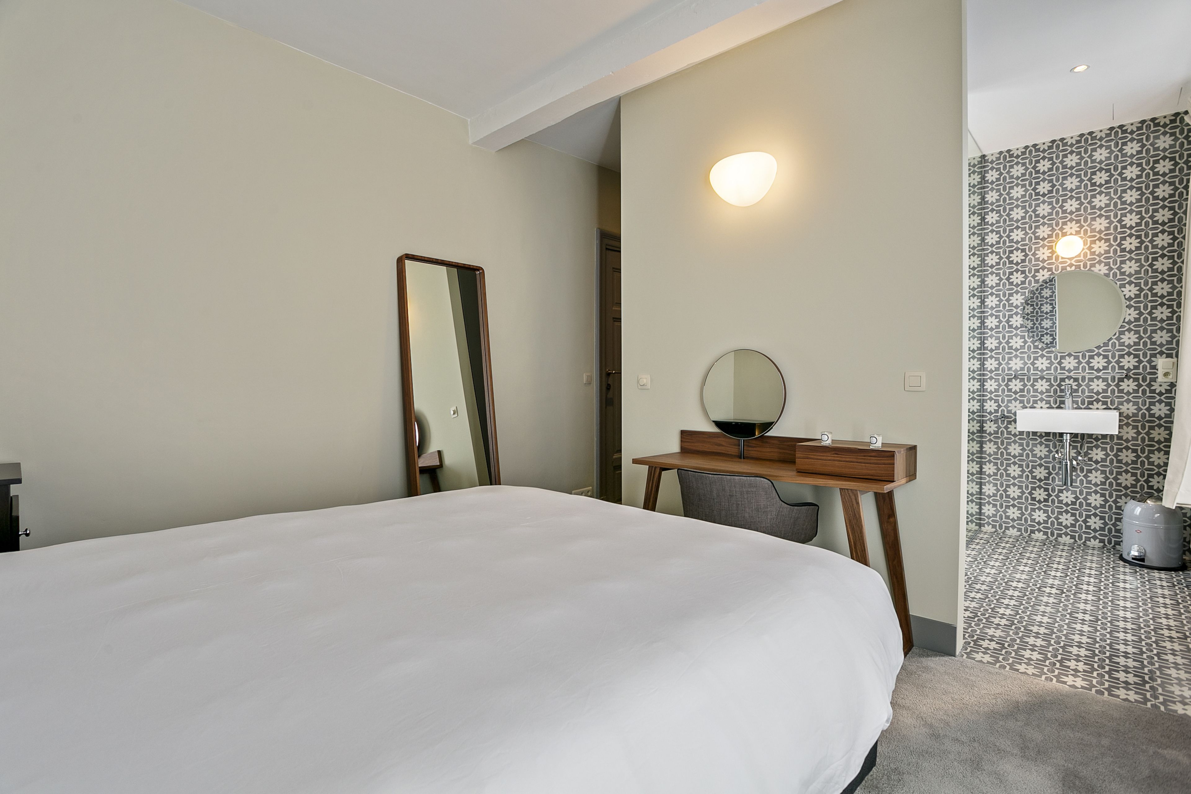 Habitación de hotel con una cama grande, un escritorio con espejo y un baño con azulejos estampados.
