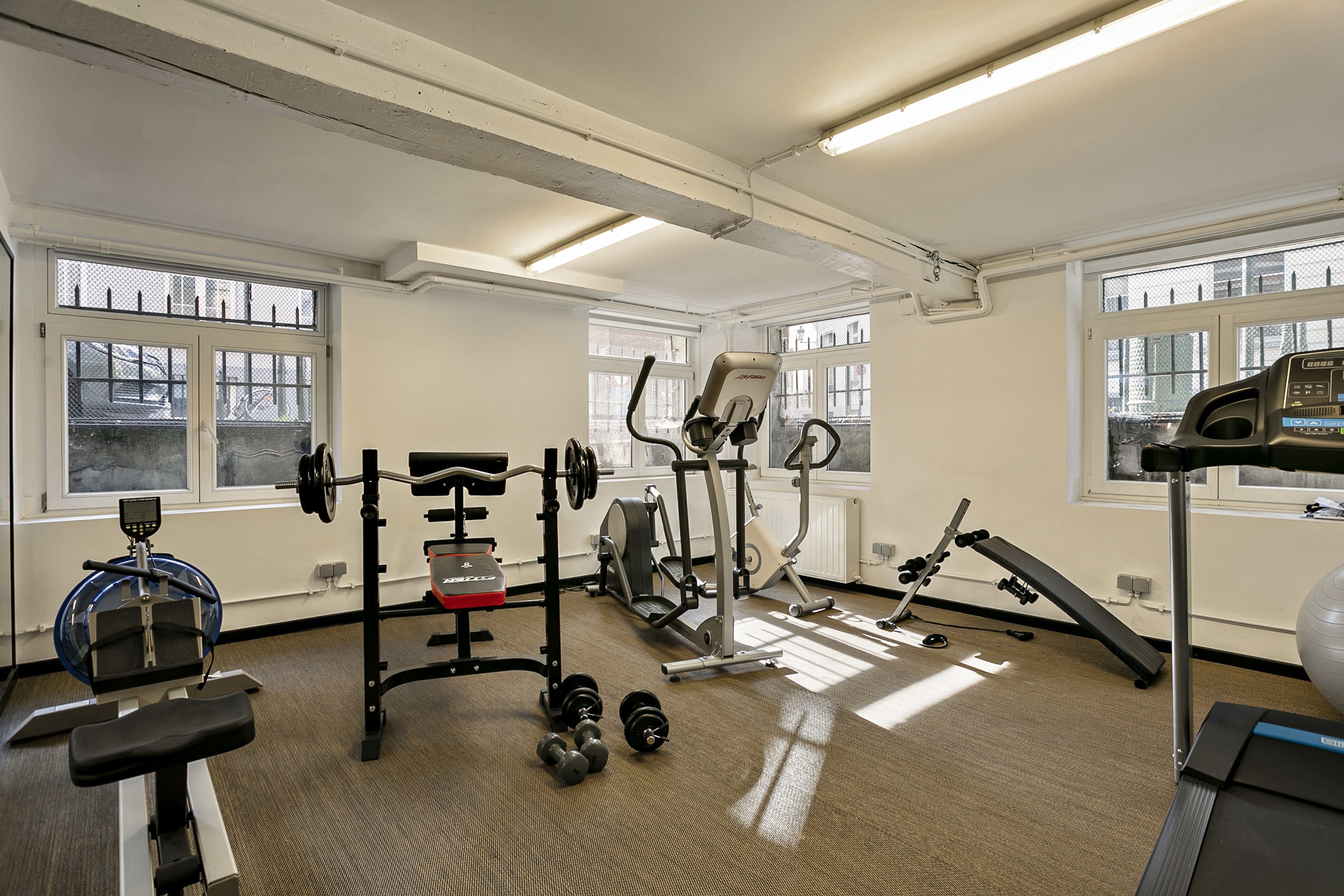 A gym with various exercise equipment, large windows, and a carpeted floor.