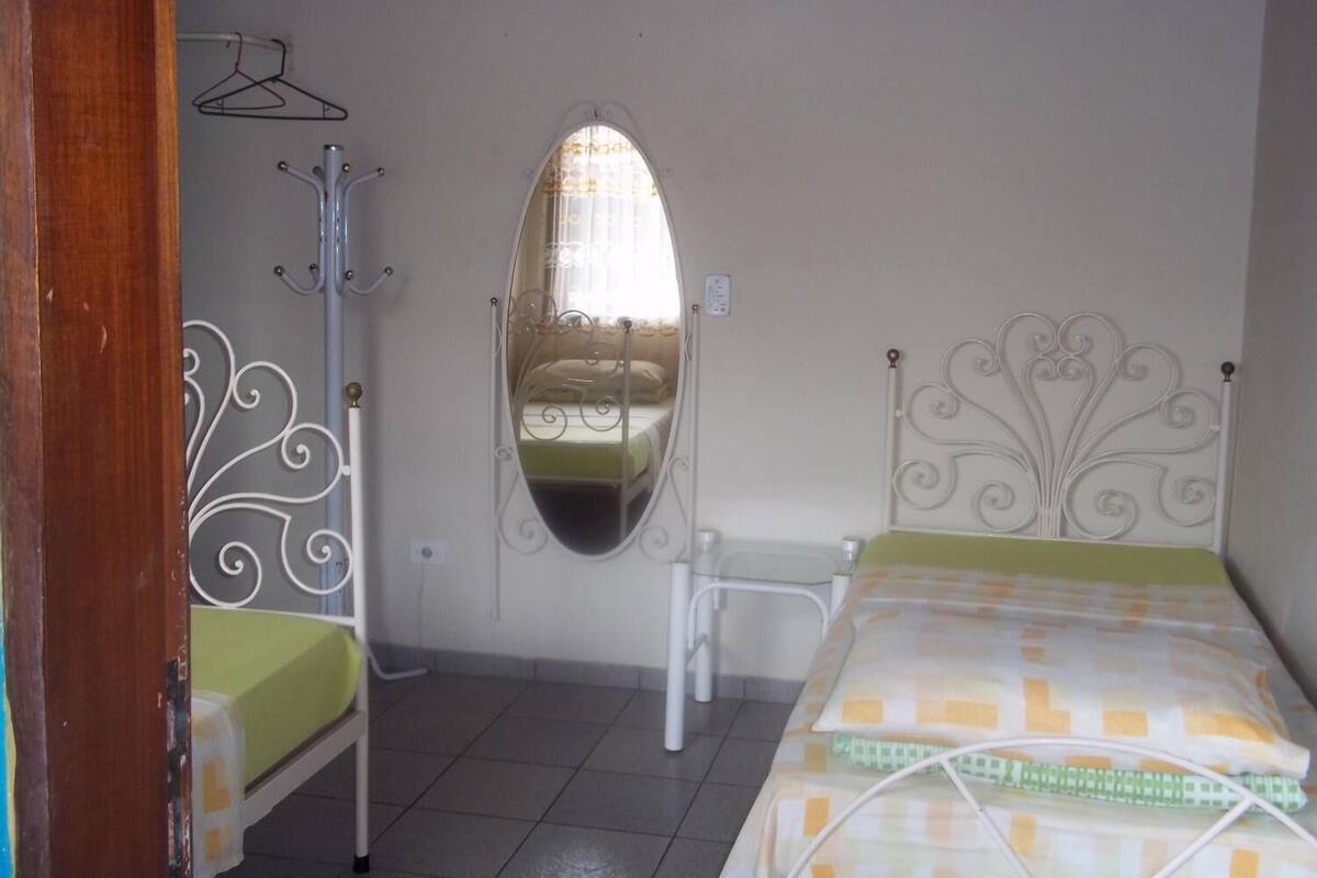 A bedroom with a bed, a chair, a coat rack, and a mirror.